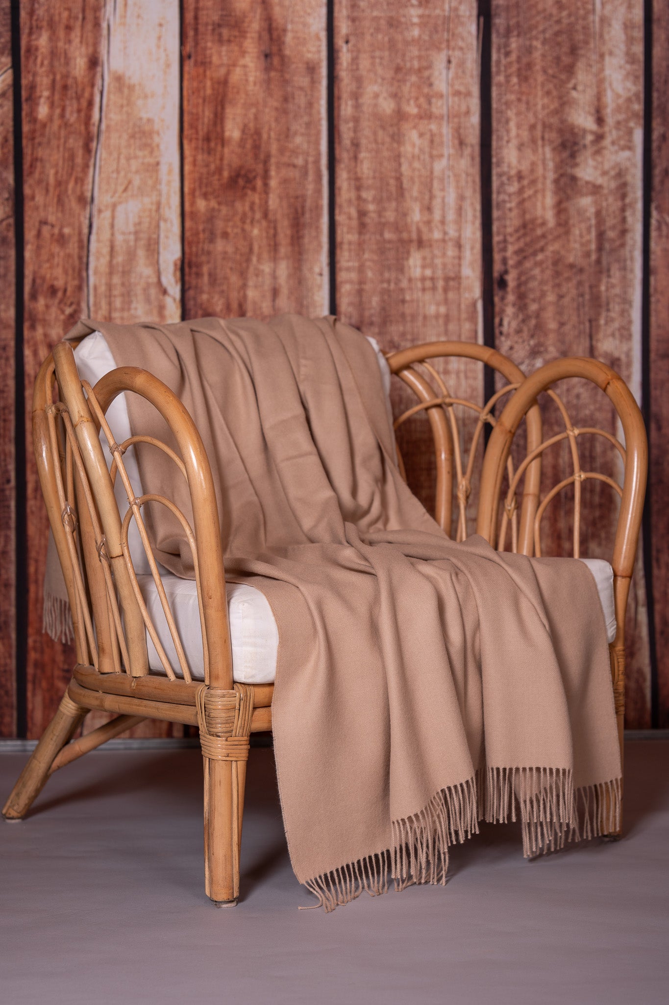 Jeté beige à franges déposé sur un fauteuil en bois